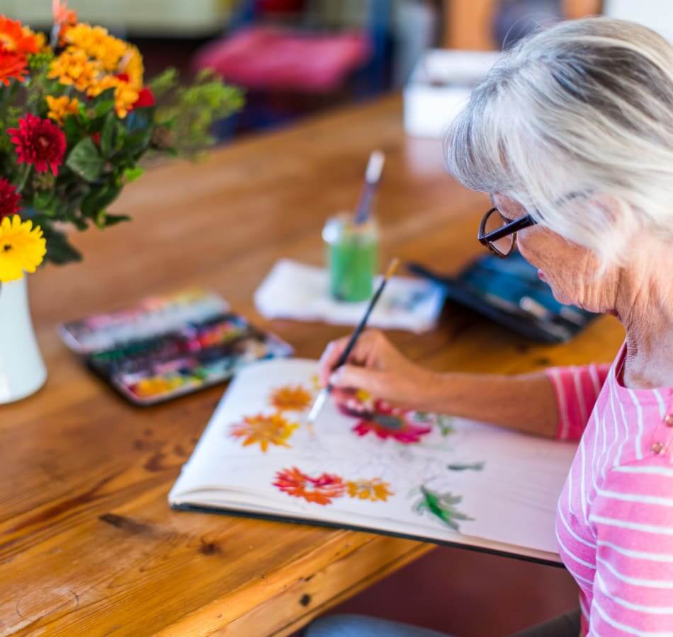 Senior woman painting colorful flowers during a creative activity.
